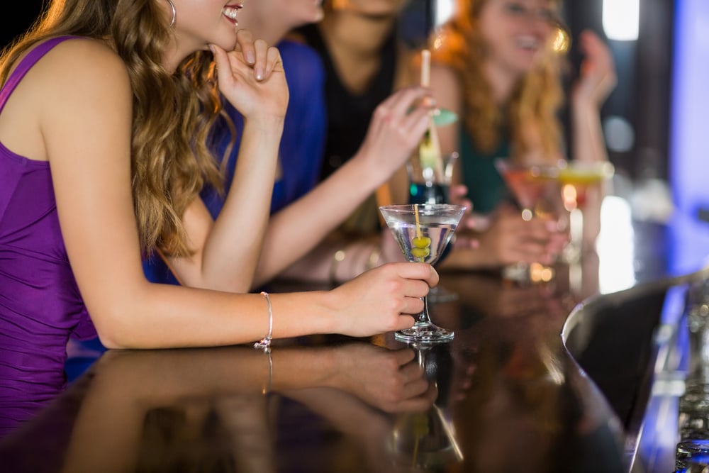 Mid section of smiling woman having glass of cocktail in bar